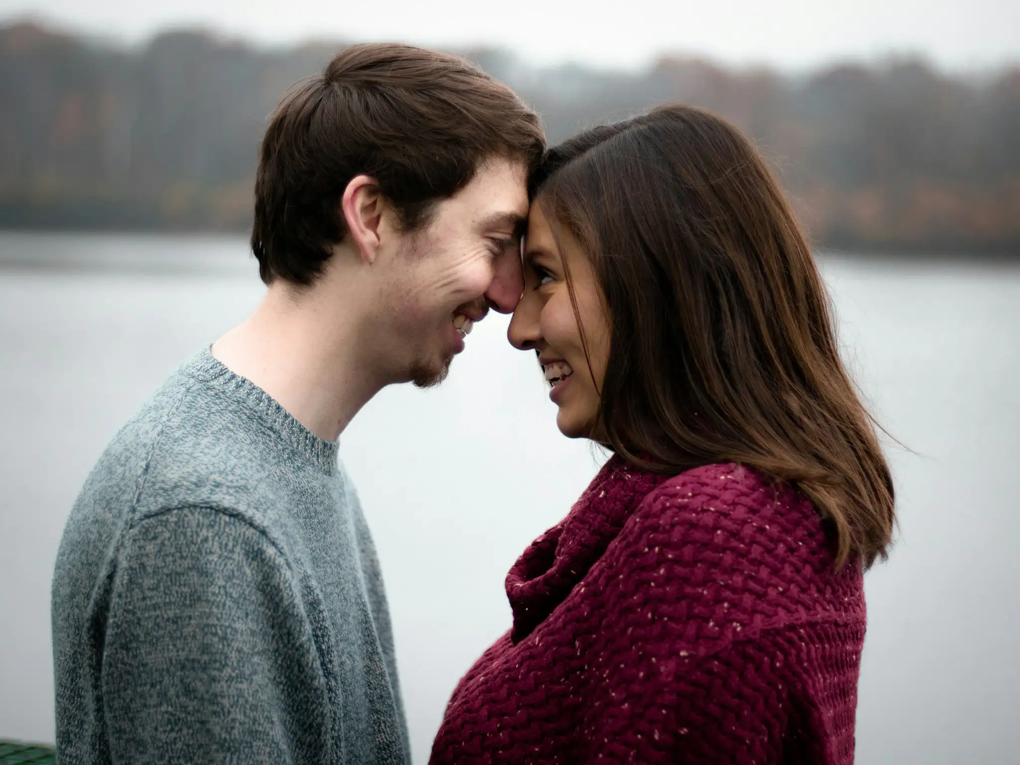 Pareja juntando sus frentes y sonriendo, junto a un lago